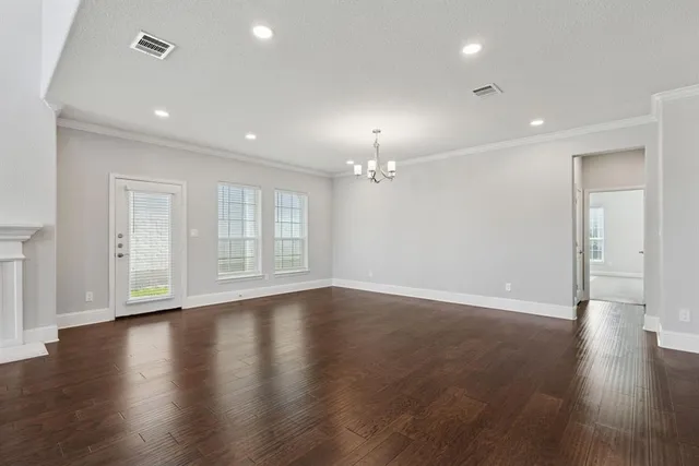 an empty room with wooden floor chandelier and windows