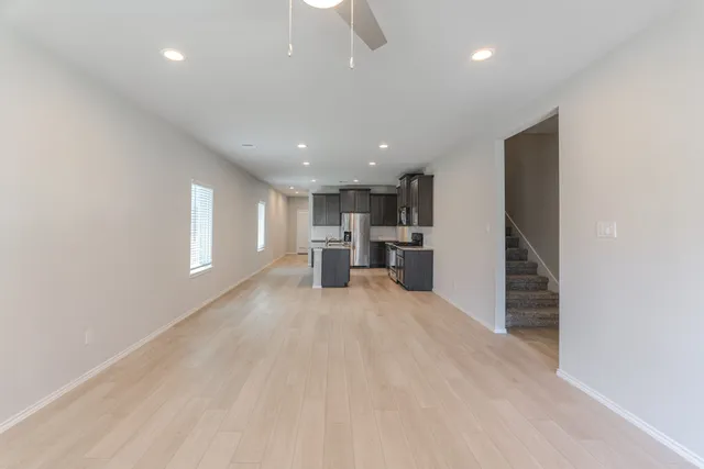 an empty room with windows and view of kitchen