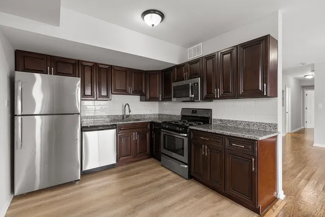 a kitchen with stainless steel appliances granite countertop a stove top oven a refrigerator a sink and dishwasher with wooden floor