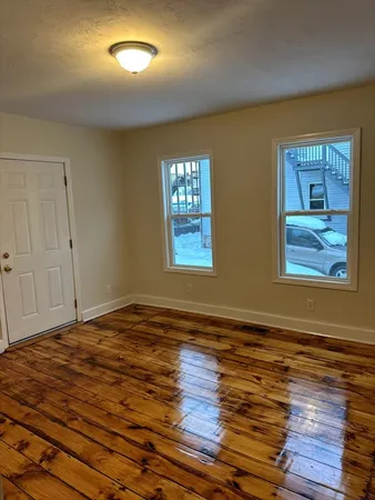 a view of an empty room with wooden floor and window