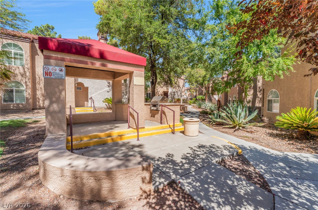 9325 West Desert Inn Road, Unit 177 Las Vegas, NV 89117 - Photo 23 of 24 An outdoor grilling area under a shaded canopy features paved walkways and mature landscaping.