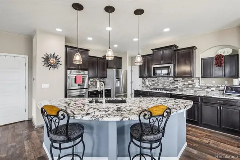 a kitchen with stainless steel appliances kitchen island granite countertop a sink a stove a kitchen island with chairs and white cabinets