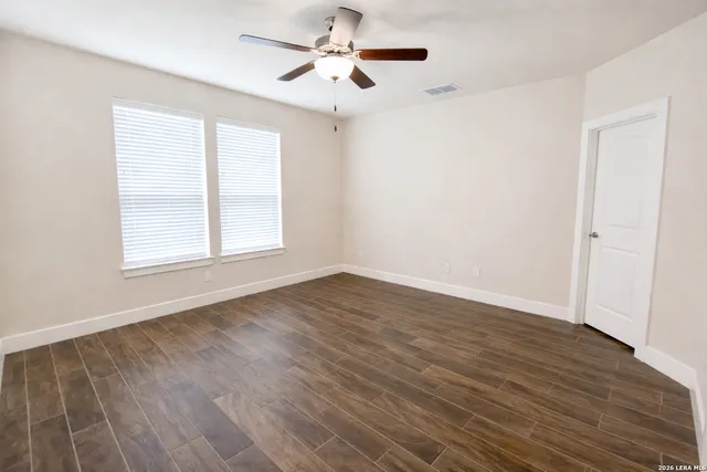 an empty room with wooden floor ceiling fan and windows