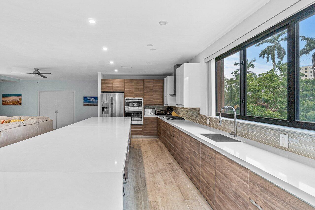 122 Andrews Avenue, Unit 2A Delray Beach, FL 33483 - Photo 10 of 39 a view of a kitchen with kitchen island a large window cabinets a sink and stainless steel appliances
