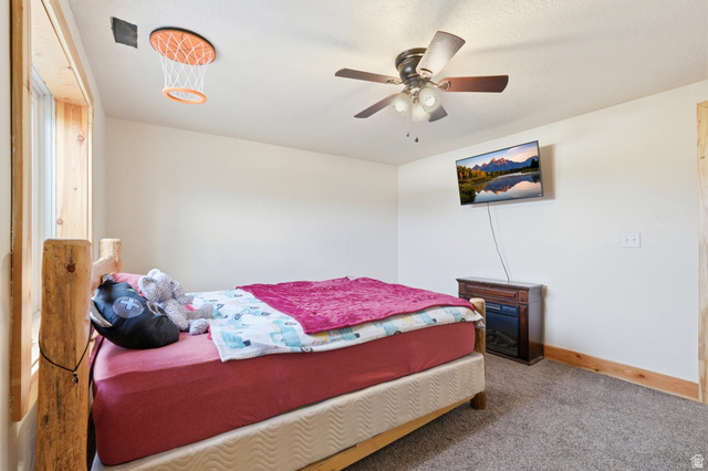 306 Spring Road Preston, ID 83263 - Photo 31 of 55 Carpeted bedroom featuring a rustic wood-frame bed, a ceiling fan with integrated lighting, a wall-mounted television, and a built-in electric fireplace