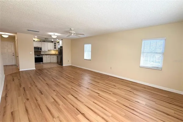 an empty room with wooden floor and kitchen view