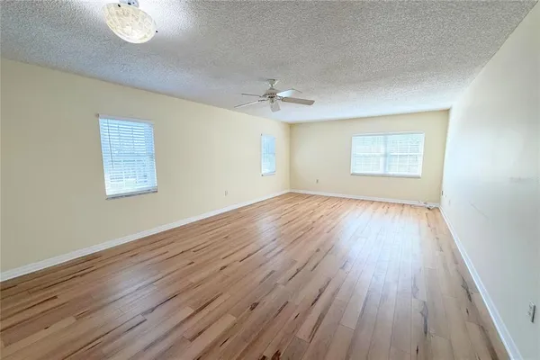 an empty room with wooden floor chandelier fan and windows