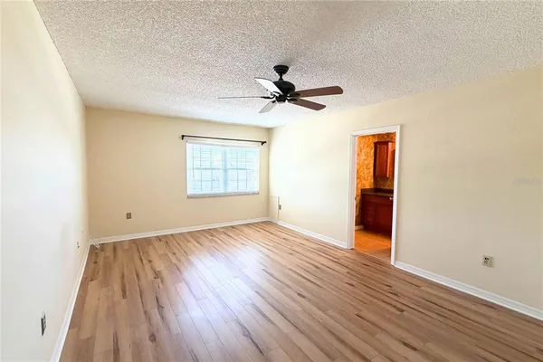 an empty room with wooden floor chandelier fan and windows
