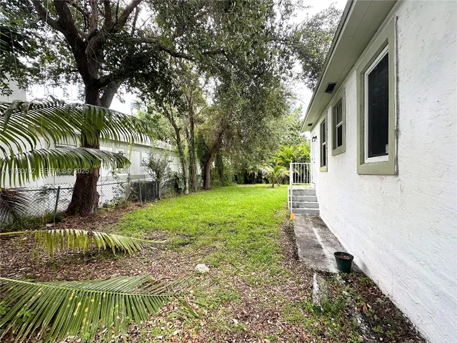 a view of a backyard with table and chairs potted plants and large tree