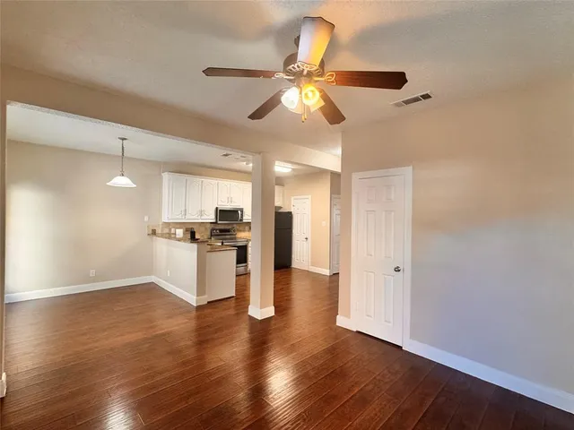 a view of an empty room and kitchen with wooden floor