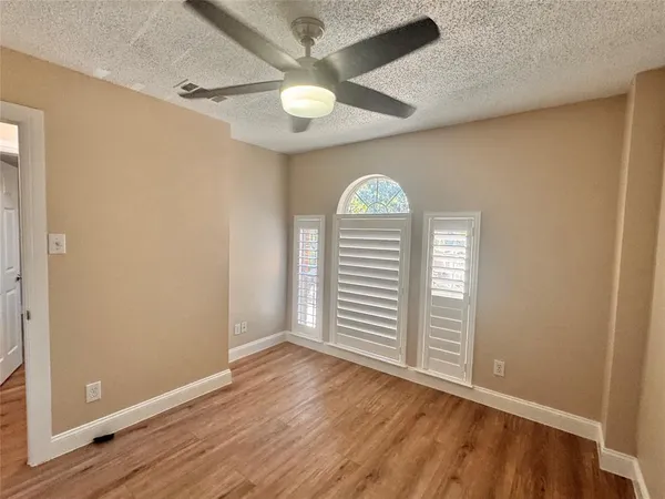an empty room with wooden floor fan and windows