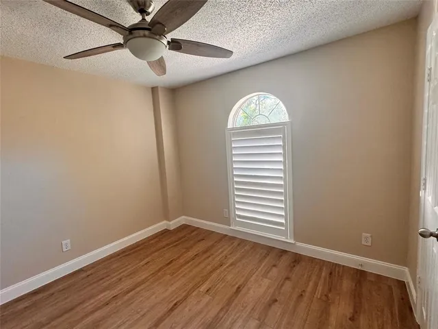 an empty room with wooden floor fan and windows