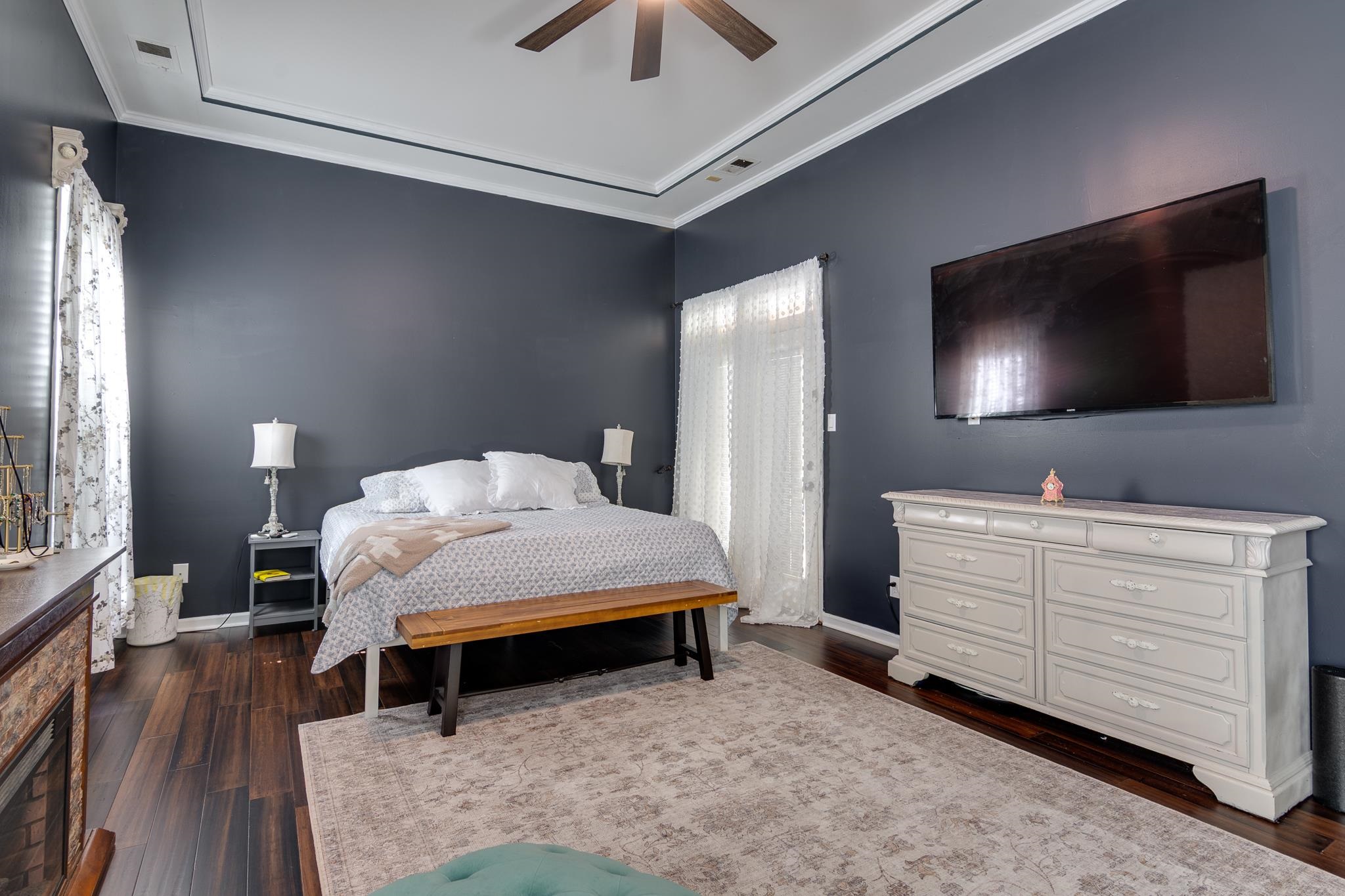 779 Early Earner Cove Collierville, TN 38017 - Photo 14 of 29 Spacious room featuring dark wood-finish flooring, a tray ceiling with crown molding, and a built-in fireplace with a stone surround