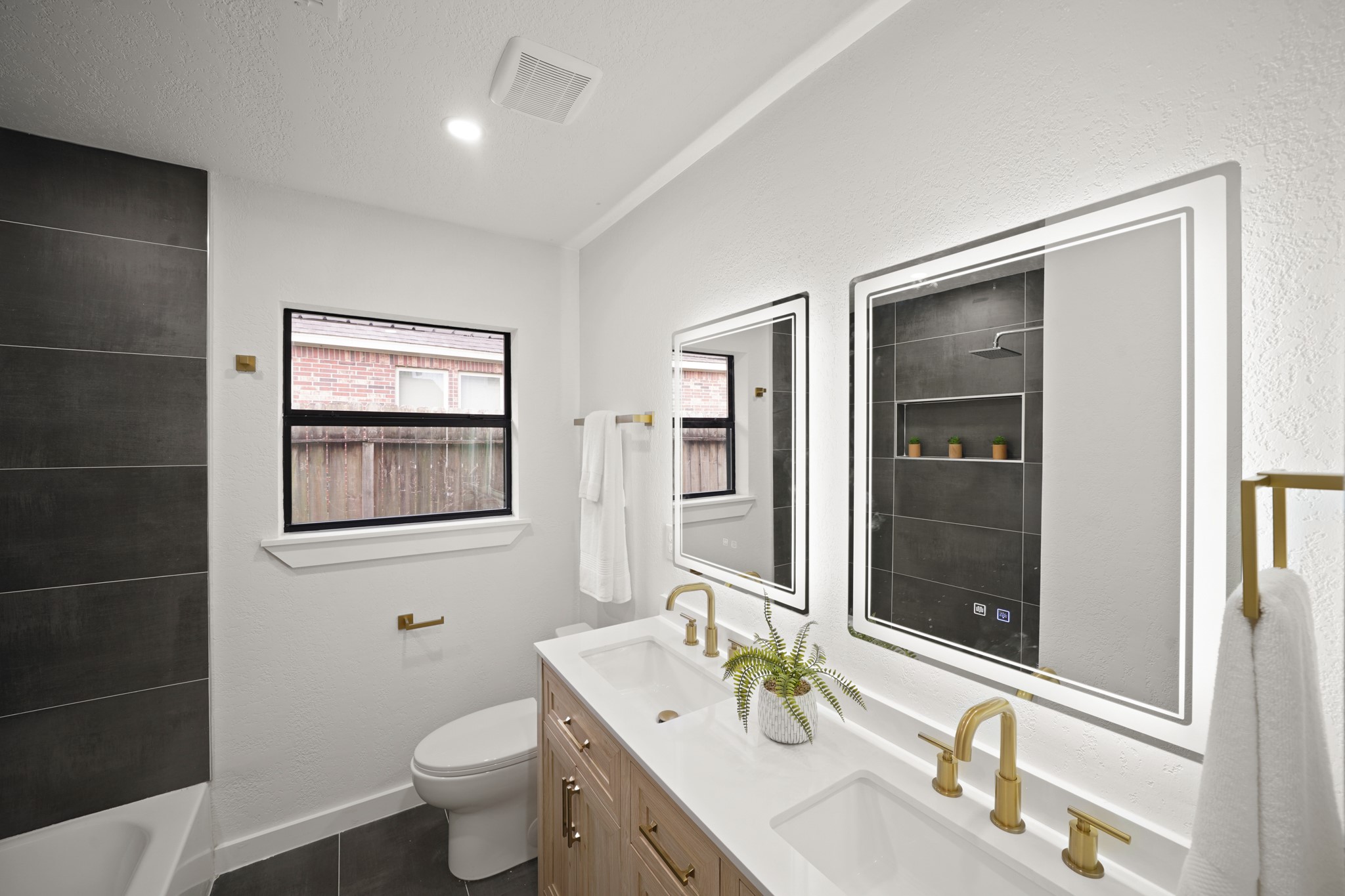 4813 Hummingbird Street Houston, TX 77035 - Photo 19 of 50 The Hall Bath (North Wing) features a Vanity w/Quartz Counters, Dual Undermount White Porcelain Sinks, Brushed Natural Brass Style Faucets, & White Oak Hued Cabinets/Drawers w/Brushed Natural Brass Hardware. The Bath also offers Dual LED Mirrors, Brushed Natural Brass Towel Rack & Paper Holder, Shelved Linen Closet w/Bifold Doors, Designer Grade Faded Concrete Tile Floors, plus a Newly installed Tub/Shower w/Metallic Grey Tile Surround, Polished Chrome Rain Shower Head, Shampoo Shelf, & LED Flush Mounts.