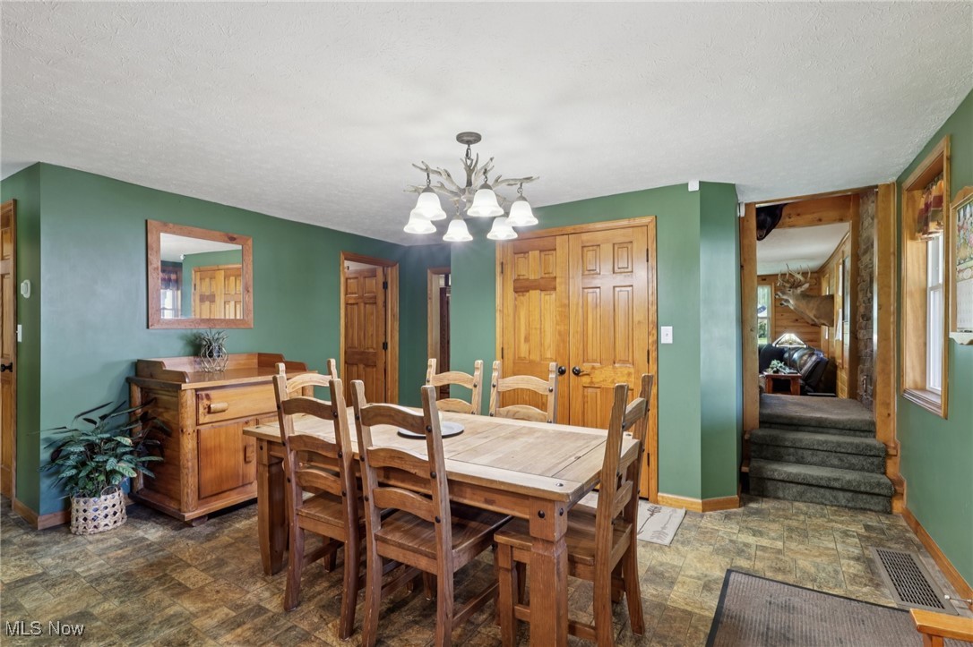 6414 Tennant Road Collins, OH 44826 - Photo 17 of 50 Dining room with stone finish flooring, a chandelier, a textured ceiling, and stairs