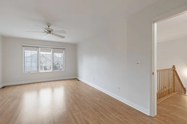 an empty room with wooden floor chandelier fan and windows
