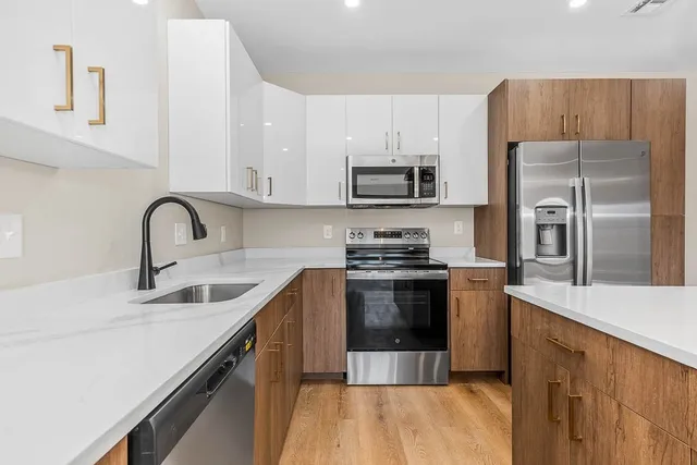 a kitchen with stainless steel appliances a sink dishwasher a refrigerator and a stove with wooden floor