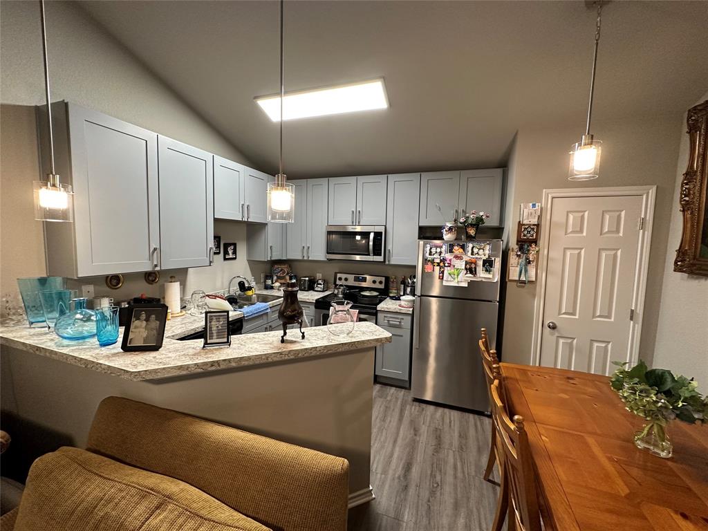 a kitchen with stainless steel appliances granite countertop a refrigerator a sink dishwasher a stove a dining table and chairs with wooden floor