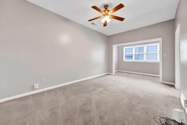 an empty room with chandelier fan and windows