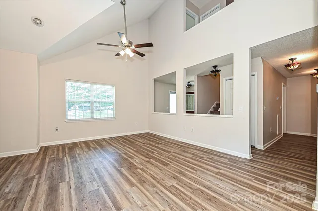 an empty room with wooden floor chandelier fan and windows