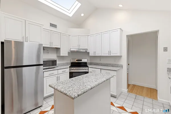 a kitchen with granite countertop a refrigerator a sink and white cabinets