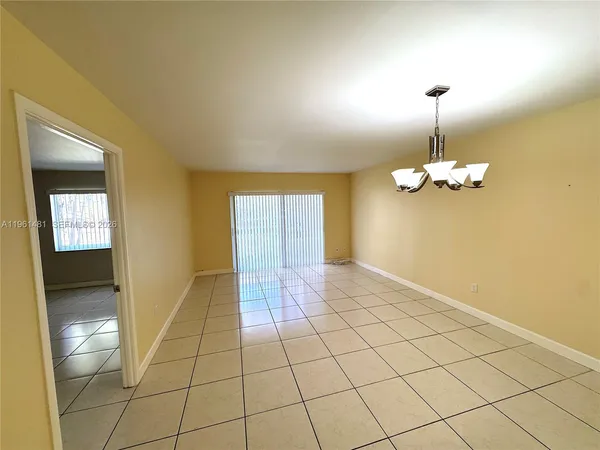 a view of an empty room with chandelier fan and kitchen view