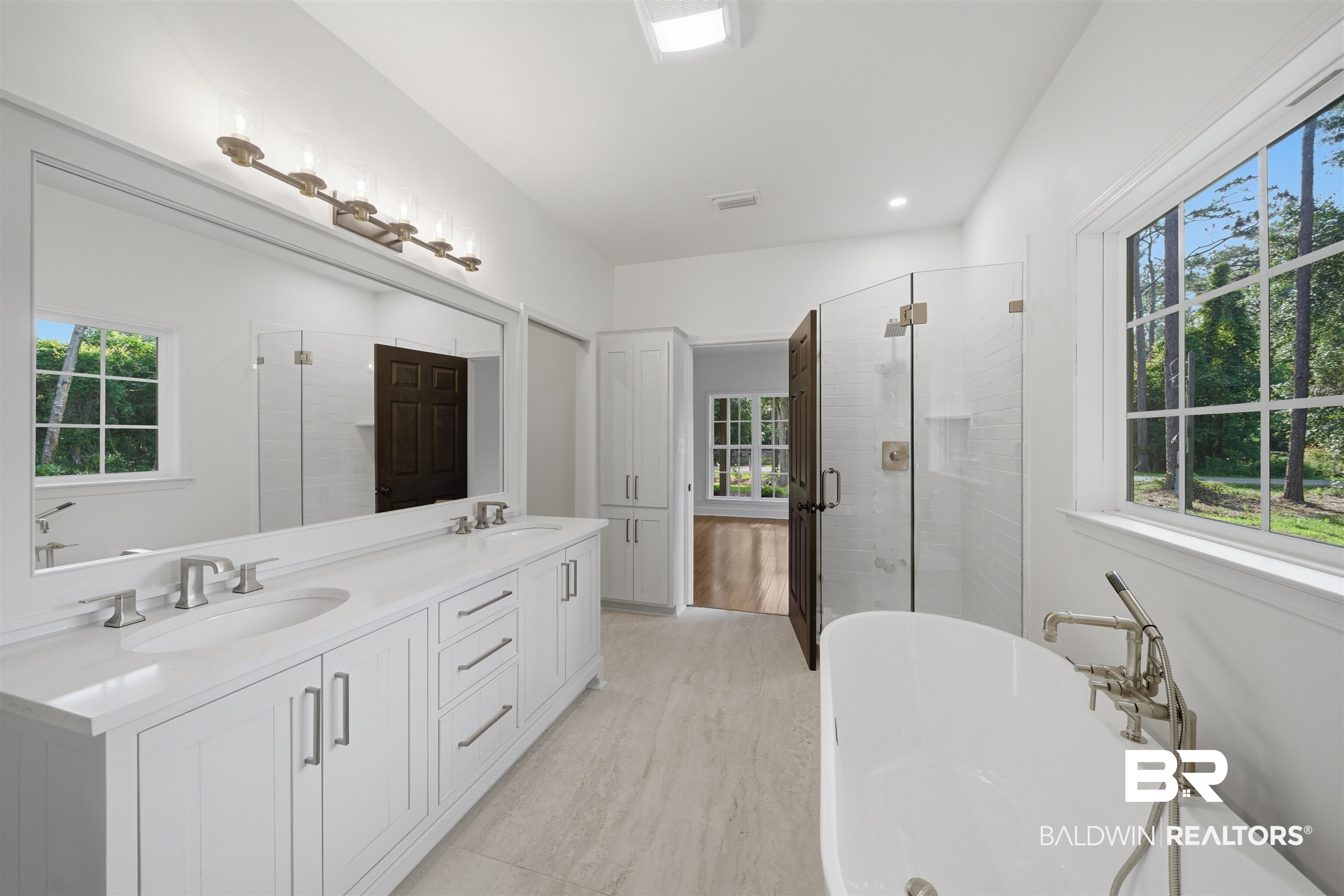 14128 Jackson Lane Foley, AL 36535 - Photo 22 of 36 Spacious bathroom featuring a dual vanity with white cabinetry and light-toned countertops, a freestanding soaking tub with floor-mounted fixtures, a glass-enclosed shower with tiled walls, large windows, and light-toned tile flooring