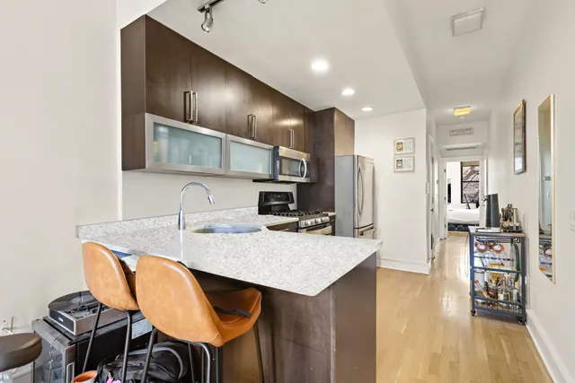 a kitchen with stainless steel appliances kitchen island granite countertop a stove a refrigerator a sink a dining table and chairs with wooden floor