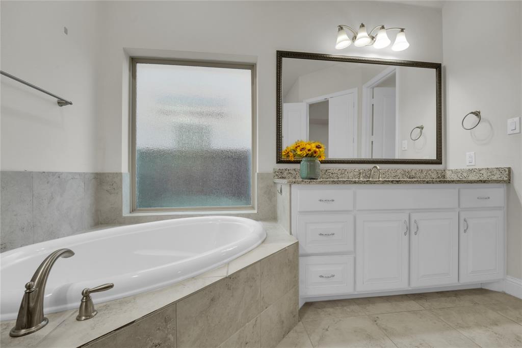 1011 Prairie Ridge Lane Arlington, TX 76005 - Photo 30 of 32 Bathroom featuring an inset soaking tub with brushed nickel fixtures, a large vanity with white cabinetry, a light-toned countertop, and a wide mirror with an ornate frame