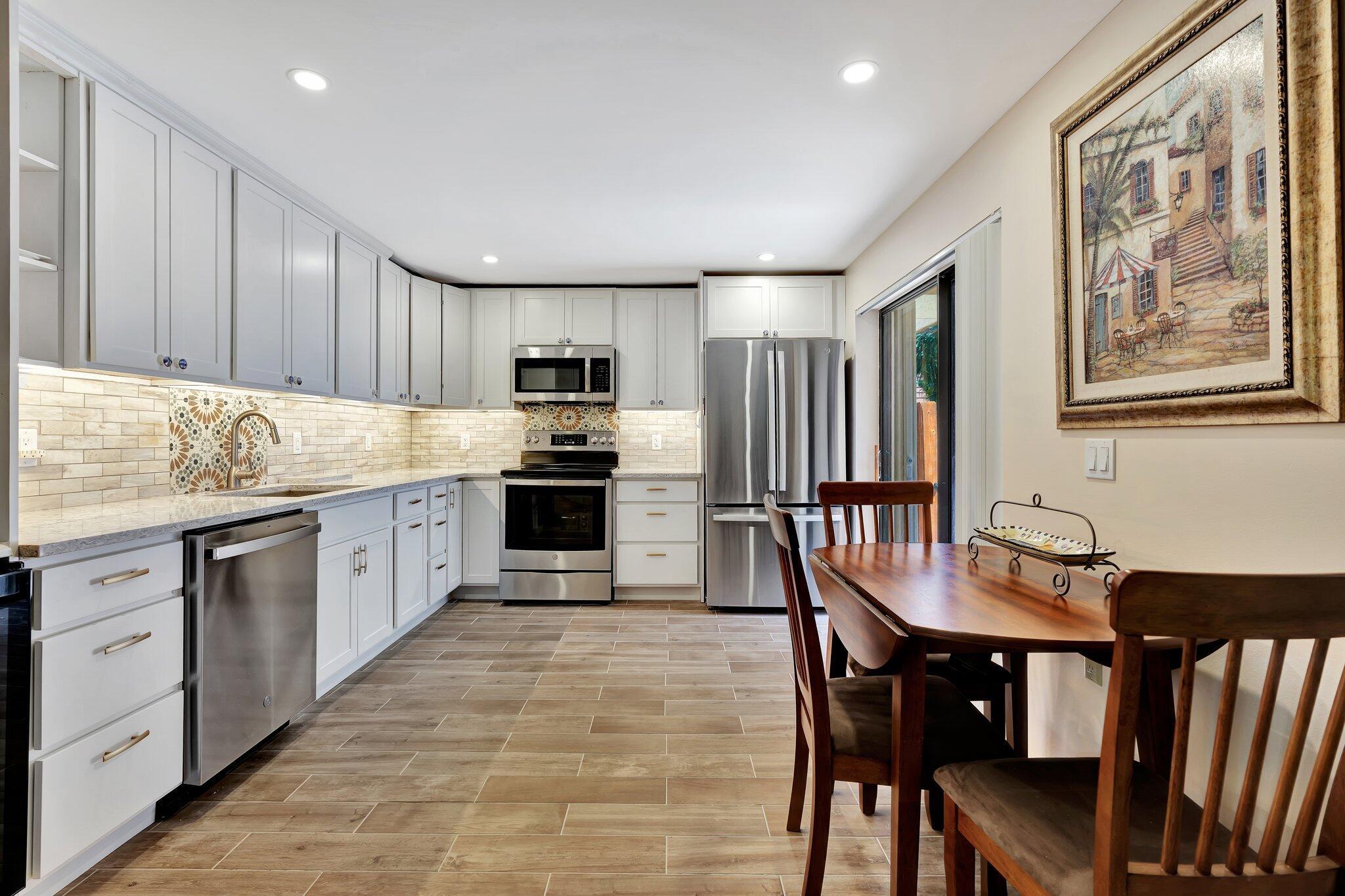 3016 30th Court Jupiter, FL 33477 - Photo 3 of 8 a open kitchen with stainless steel appliances granite countertop a stove a sink dishwasher a dining table and chairs