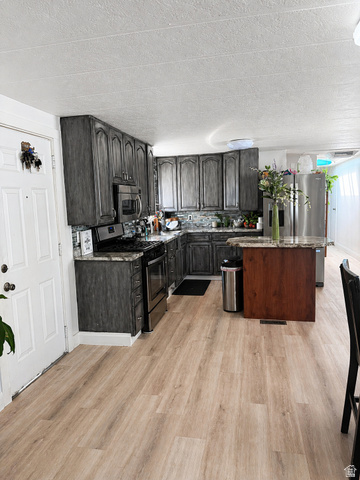 33 Apollo Way Sandy, UT 84070 - Photo 6 of 9 Kitchen with stainless steel appliances, a center island, light wood-style flooring, a textured ceiling, and dark stone counters