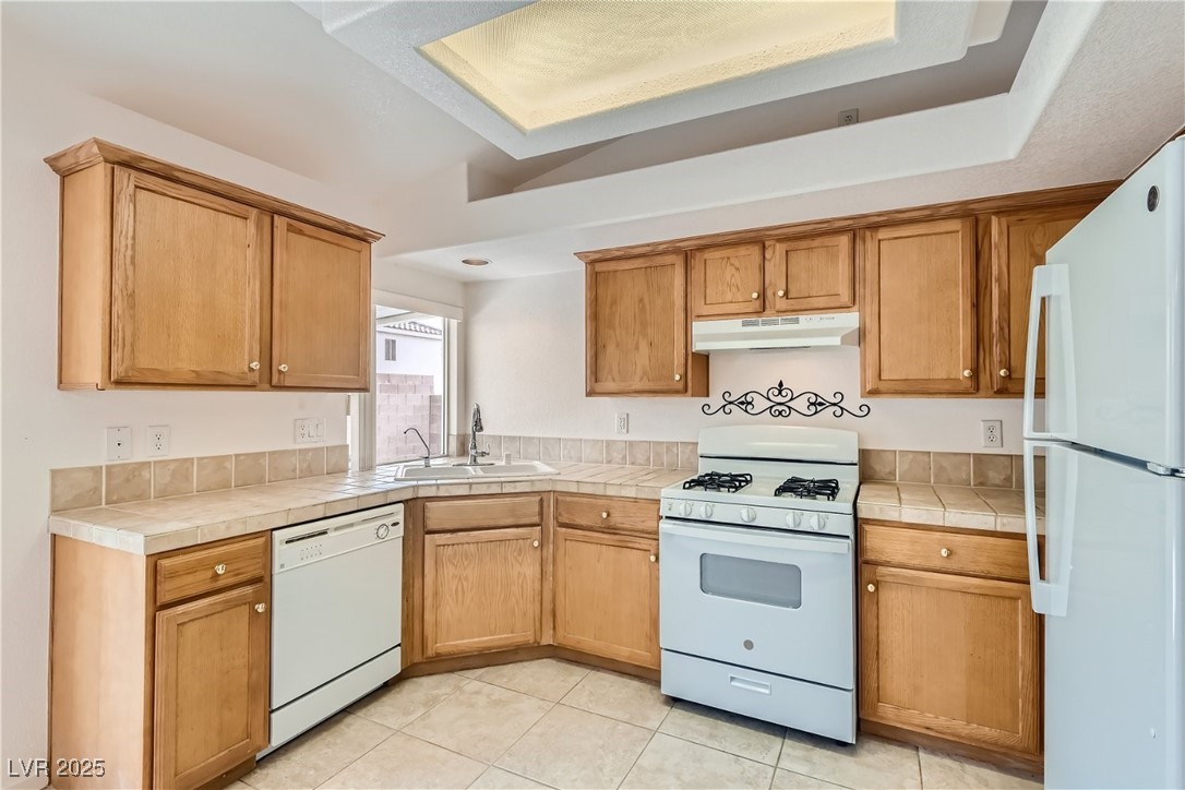 7550 Slipstream Street Las Vegas, NV 89139 - Photo 16 of 33 Kitchen featuring white appliances, light tile patterned flooring, under cabinet range hood, and brown cabinetry