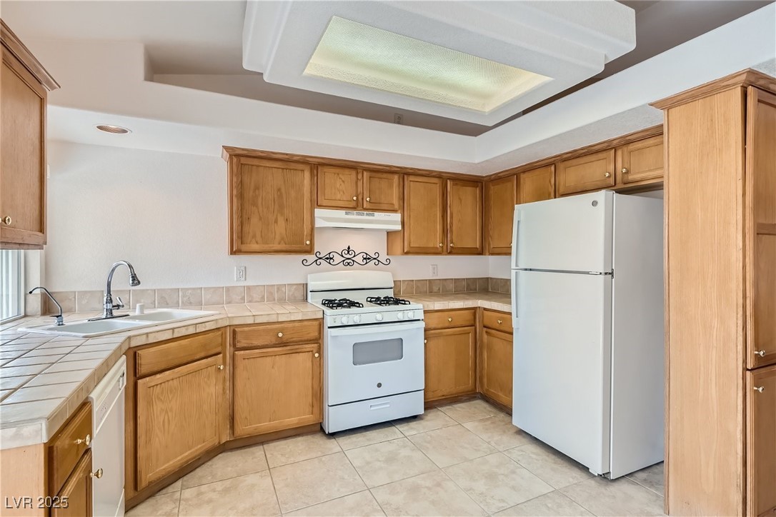 7550 Slipstream Street Las Vegas, NV 89139 - Photo 17 of 33 Kitchen featuring white appliances, light tile patterned flooring, tile counters, brown cabinetry, and under cabinet range hood