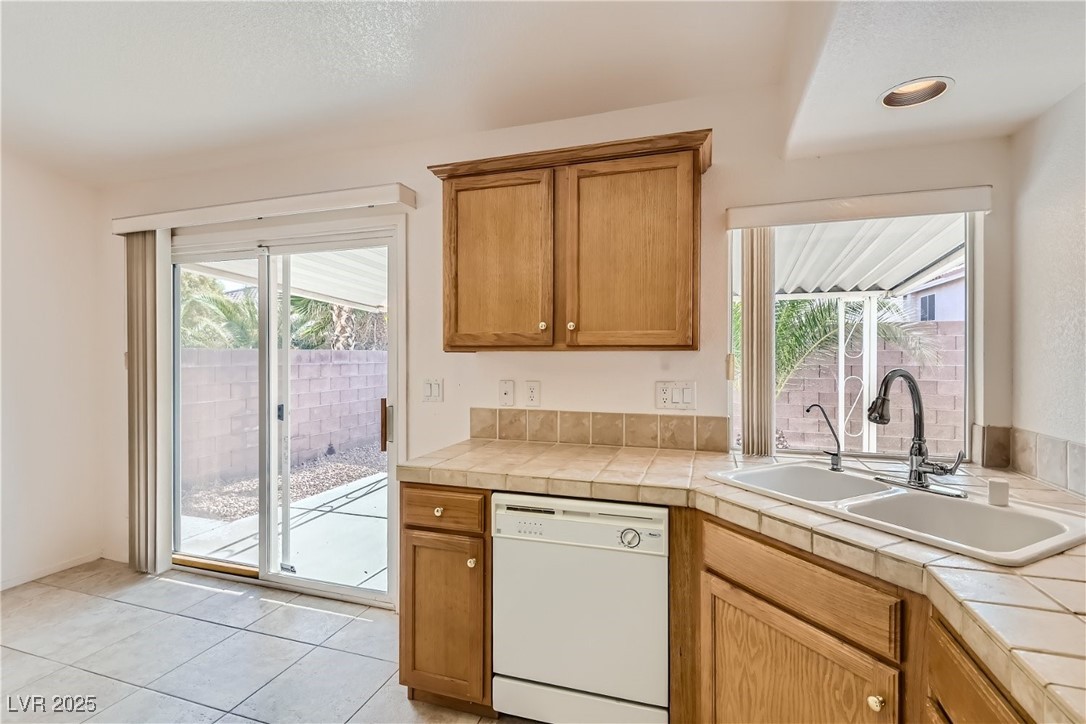 7550 Slipstream Street Las Vegas, NV 89139 - Photo 18 of 33 Kitchen featuring white dishwasher, light tile patterned floors, tile counters, and brown cabinetry