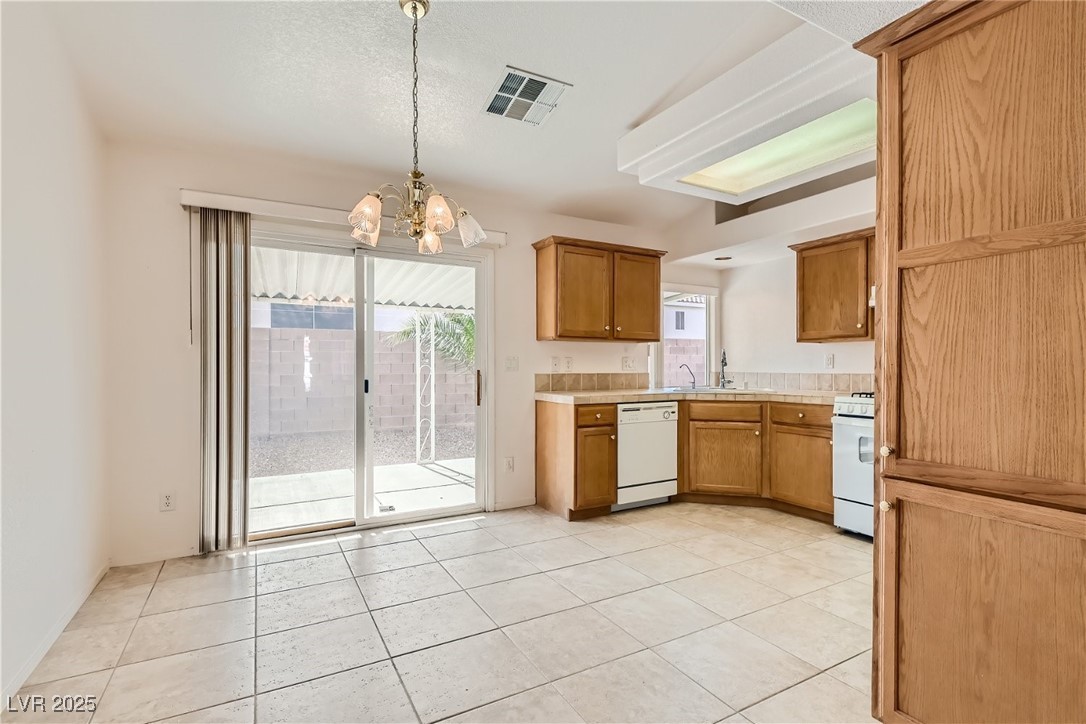 7550 Slipstream Street Las Vegas, NV 89139 - Photo 19 of 33 Kitchen featuring brown cabinetry, a chandelier, light tile patterned floors, pendant lighting, and white appliances