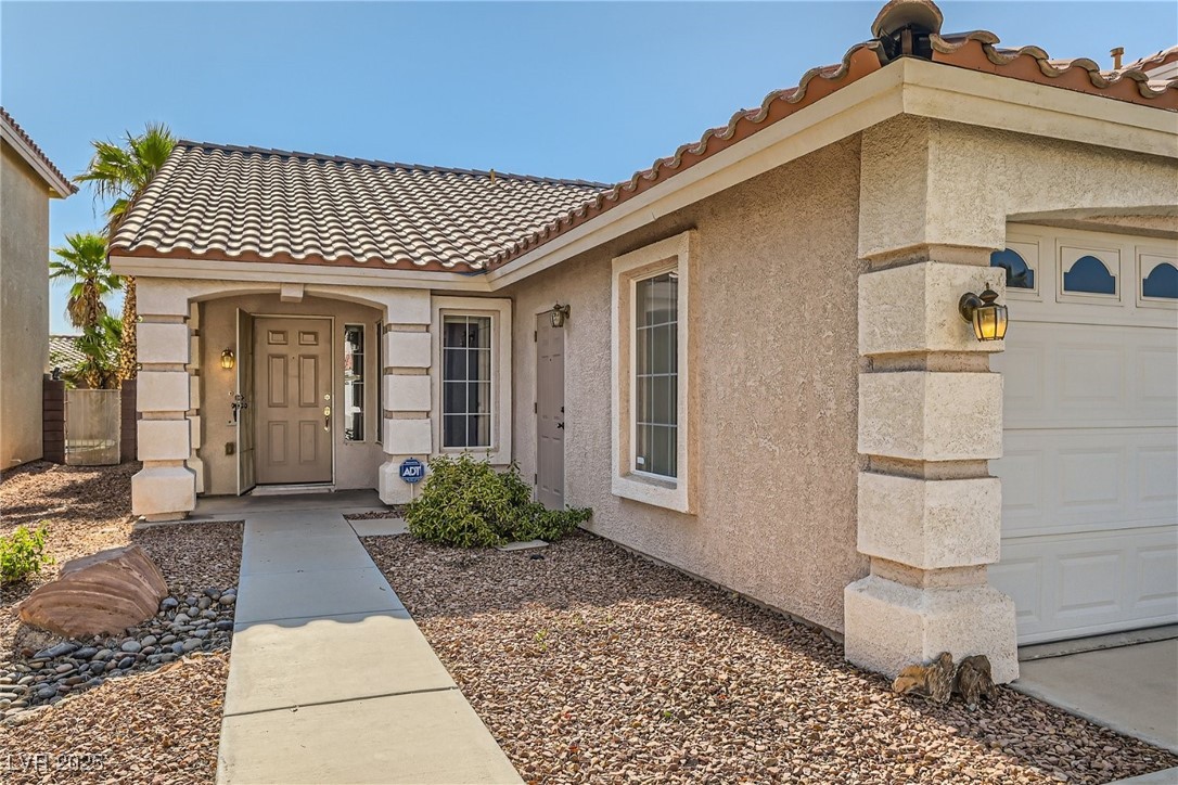 7550 Slipstream Street Las Vegas, NV 89139 - Photo 9 of 33 View of exterior entry featuring a tiled roof, stucco siding, and an attached garage