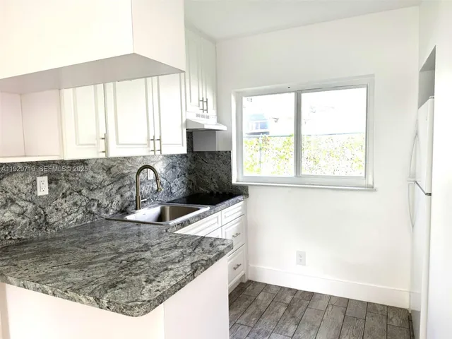 a kitchen with granite countertop a sink a window and cabinets