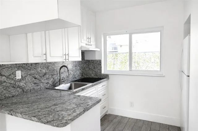 a kitchen with granite countertop a sink a window and cabinets