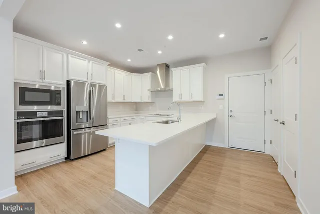 a large kitchen with a center island wooden floor and stainless steel appliances