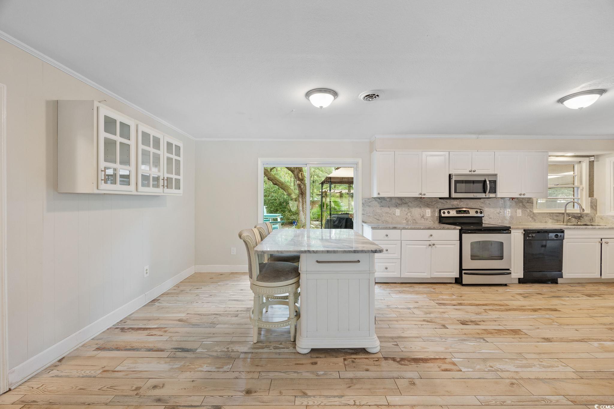 4303 Old Kings Highway Murrells Inlet, SC 29576 - Photo 8 of 34 Kitchen with stainless steel appliances, tasteful backsplash, white cabinets, crown molding, and light wood-style flooring