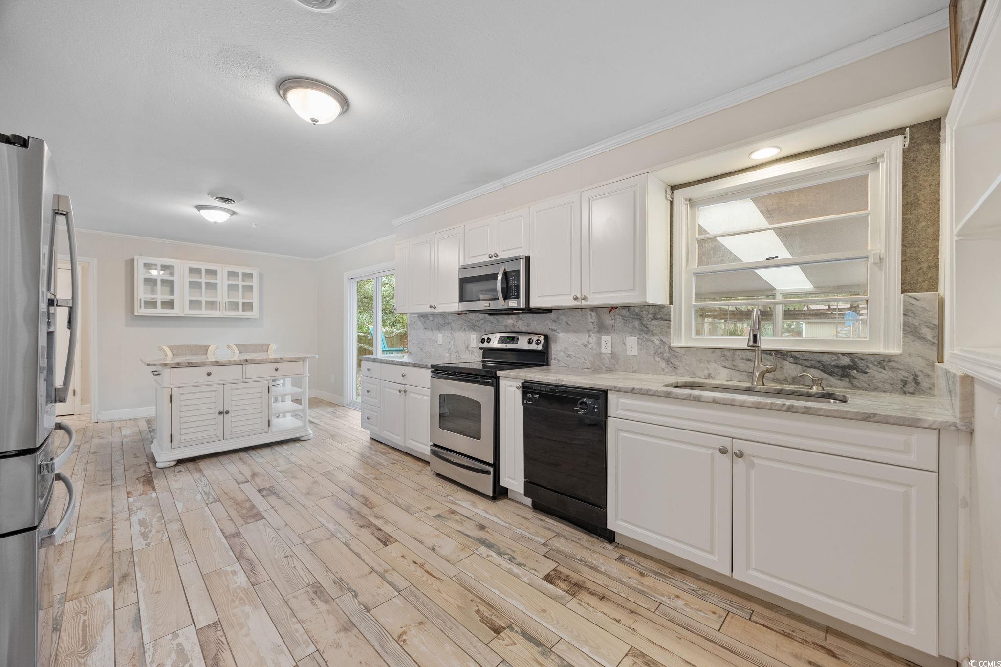 4303 Old Kings Highway Murrells Inlet, SC 29576 - Photo 9 of 34 Kitchen with stainless steel appliances, tasteful backsplash, crown molding, light wood-type flooring, and white cabinets