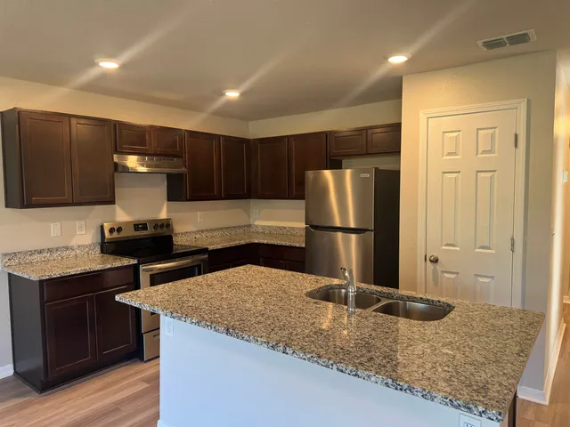 a kitchen with kitchen island granite countertop a sink and a refrigerator