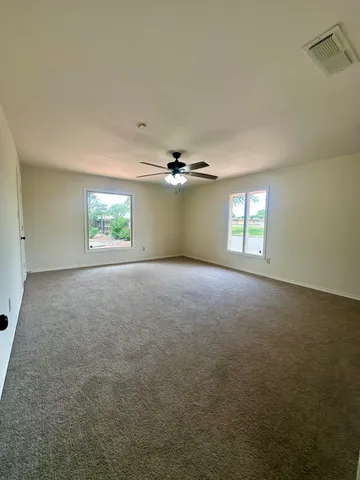an empty room with a chandelier fan and windows