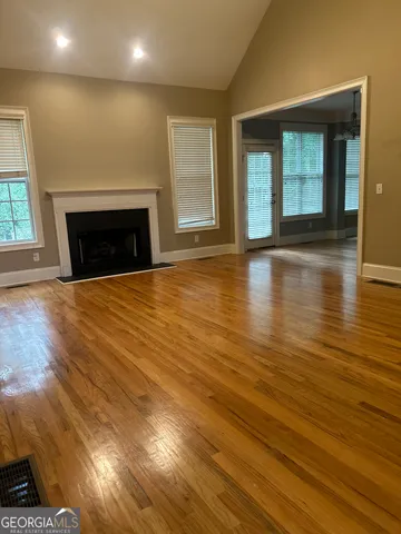 an empty room with wooden floor fireplace and windows