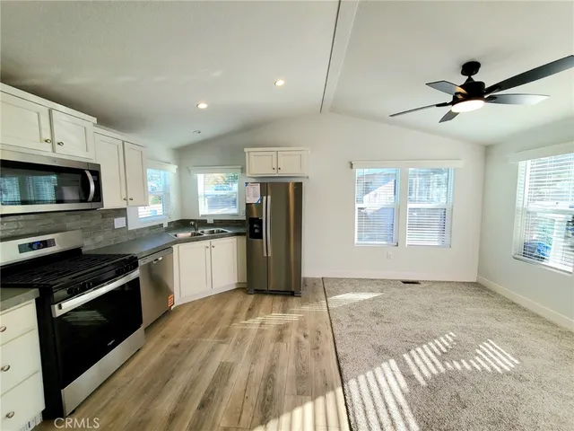 a kitchen with granite countertop a stove top oven a sink dishwasher a refrigerator and white cabinets with wooden floor