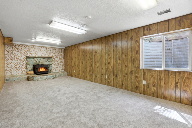 2348 North 770 West Clinton, UT 84015 - Photo 12 of 25 Spacious room featuring wood paneling, light gray carpeting, and a stone fireplace with a wood-burning insert