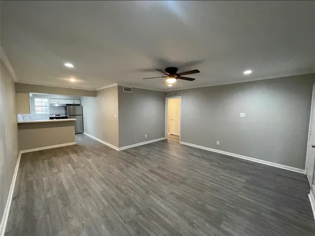 a view of an empty room with wooden floor and a kitchen