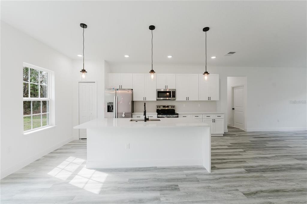 6732 Southwest 132nd Street Ocala, FL 34473 - Photo 11 of 36 a white kitchen with stainless steel appliances kitchen island granite countertop a stove a sink a refrigerator and white cabinets with wooden floor