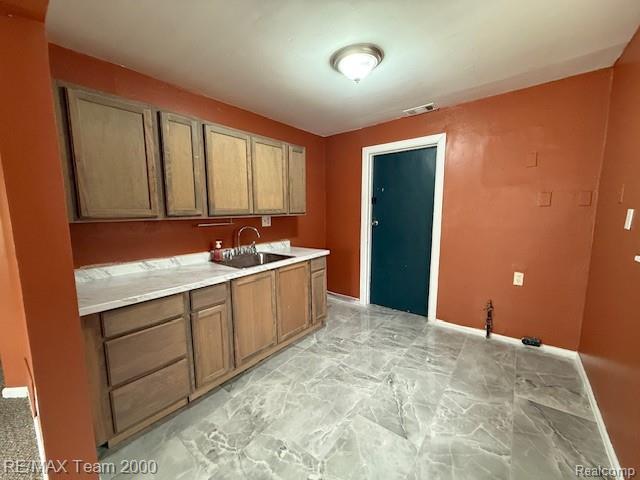26174 Kitch Street Inkster, MI 48141 - Photo 5 of 8 Kitchen area featuring wood cabinetry, a stainless steel sink with a chrome faucet, light-toned countertop, and grey marble-look tile flooring