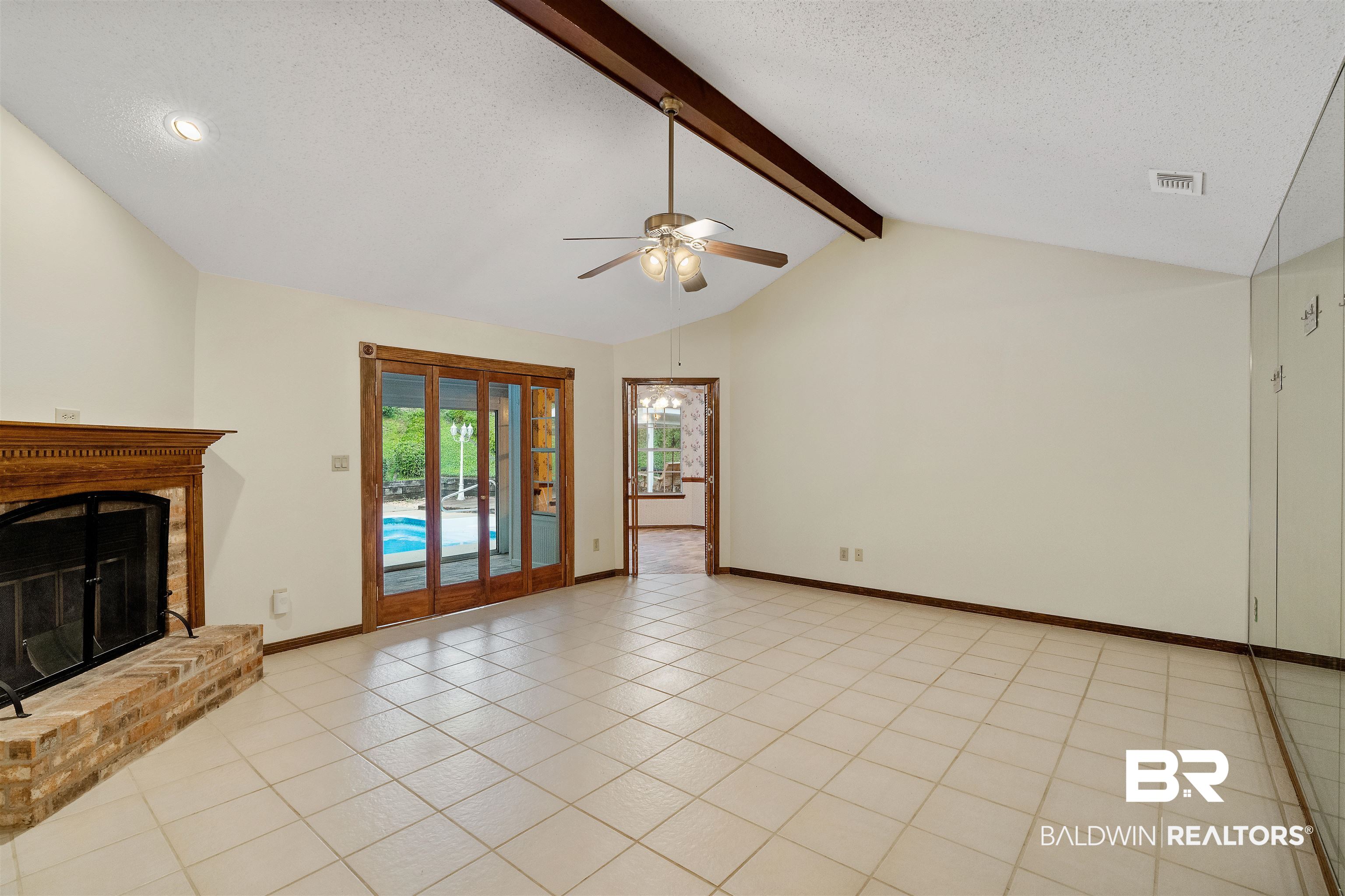 438 Ridgewood Drive Daphne, AL 36526 - Photo 6 of 28 Unfurnished living room featuring ceiling fan, light tile patterned floors, a brick fireplace, a textured ceiling, and lofted ceiling with beams
